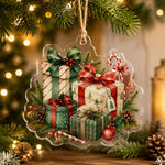 Clear acrylic Christmas ornament featuring a watercolor illustration of stacked presents, pinecones, and red berries.
