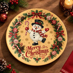 Cream charger plate with gold trim featuring a snowman inside a fir wreath and a red ribbon bow