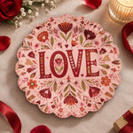Pink scalloped plate with deep wine LOVE letters among oxblood flowers