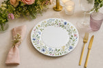 * Elegant white floral charger plates styled on a wedding reception dinner table with upscale glassware and linens.