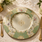 Sage green decorative charger plate with ornate gold filigree border, pastel floral sprays and a central gold medallion, top-down view.