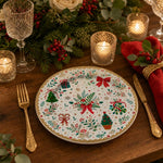 Christmas decorative charger plate with scattered holiday trees, gifts, red bows and holly on cream base with gold scalloped rim, top-down view.