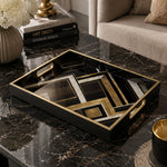 Art Deco decorative tray with black, gold, and marble geometric design framed in a black tray with gold rim and electroplated handles, styled on a black marble coffee table beside white hydrangeas, brass decor, and Art Deco design books.