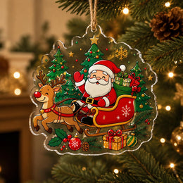 Clear acrylic Christmas hanging ornament featuring Santa in his red sleigh with reindeer and decorated pine trees.
