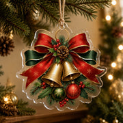 Clear acrylic Christmas hanging ornament with golden bells and red bow hanging on a pine tree branch.