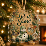 Let it Snow clear acrylic hanging ornament with a snowman, lantern, and pine branches hanging from a tree.