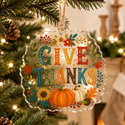 Give Thanks acrylic hanging decoration with pumpkins and sunflowers hung on a lighted holiday tree with jute twine.