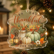 Scalloped clear acrylic hanging decor with thankful text and pumpkins, hanging on a pine branch with jute twine.