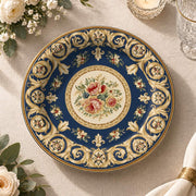 Navy blue charger plate with gold trim featuring a rose medallion and fleur-de-lis scroll border