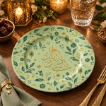 Sage green charger plate with gold trim featuring Arabic calligraphy among gold sprigs and lanterns