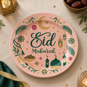Pink charger plate with gold trim featuring Eid script, a mosque and a lantern among leaves