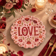 Pink scalloped plate with deep wine LOVE letters among oxblood flowers