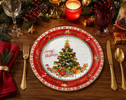 Red holiday charger plate styled on a festive dinner table with gold cutlery, red napkins, candles, and pine branches.