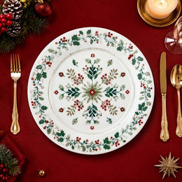 * Flat lay of a white Christmas charger plate featuring a festive green pine and red berry border design.