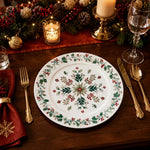 * White holiday charger plate set on a decorated Christmas dinner table with red napkins and gold cutlery.