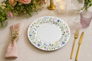 * Elegant white floral charger plates styled on a wedding reception dinner table with upscale glassware and linens.