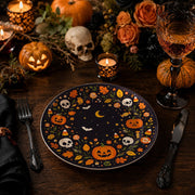 * Halloween charger plate with pumpkins, skulls, and bats on a dark dinner table setting with gold cutlery.