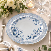 * Dusty blue floral glass charger plate set on a matching botanical tablecloth with silver cutlery and crystal glasses.
