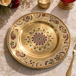 Gold electroplated Diwali charger plate with a maroon and ivory heritage mandala, jade teardrop accents and paisley scrollwork on a dining table.