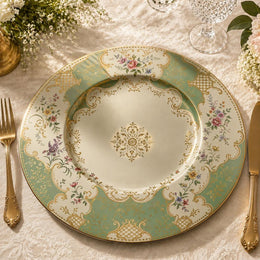 Sage green decorative charger plate with ornate gold filigree border, pastel floral sprays and a central gold medallion, top-down view.