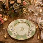 Sage green decorative charger plate with ornate gold filigree border, pastel floral sprays and a central gold medallion, top-down view.