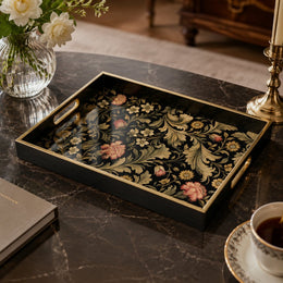 William Morris decorative tray with vintage botanical pattern of acanthus leaves and coral blossoms on a black glass base, framed by a black tray with gold electroplated rim and handles, styled on a black marble table with white roses, a brass candlestick, and an espresso cup.