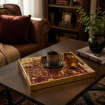 Sports Heritage Glass Serving Tray – Burgundy Gold Icons styled on a console table with a ceramic mug and books beside a brass lamp.