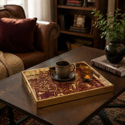 Sports Heritage Glass Serving Tray – Burgundy Gold Icons styled on a console table with a ceramic mug and books beside a brass lamp.