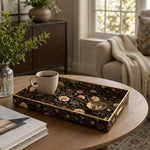 Black Gold Floral Plastic Serving Tray – Pink Chrysanthemum styled on a coffee table with books, a candle, and decorative accessories.