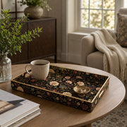 Black Gold Floral Plastic Serving Tray – Pink Chrysanthemum styled on a coffee table with books, a candle, and decorative accessories.